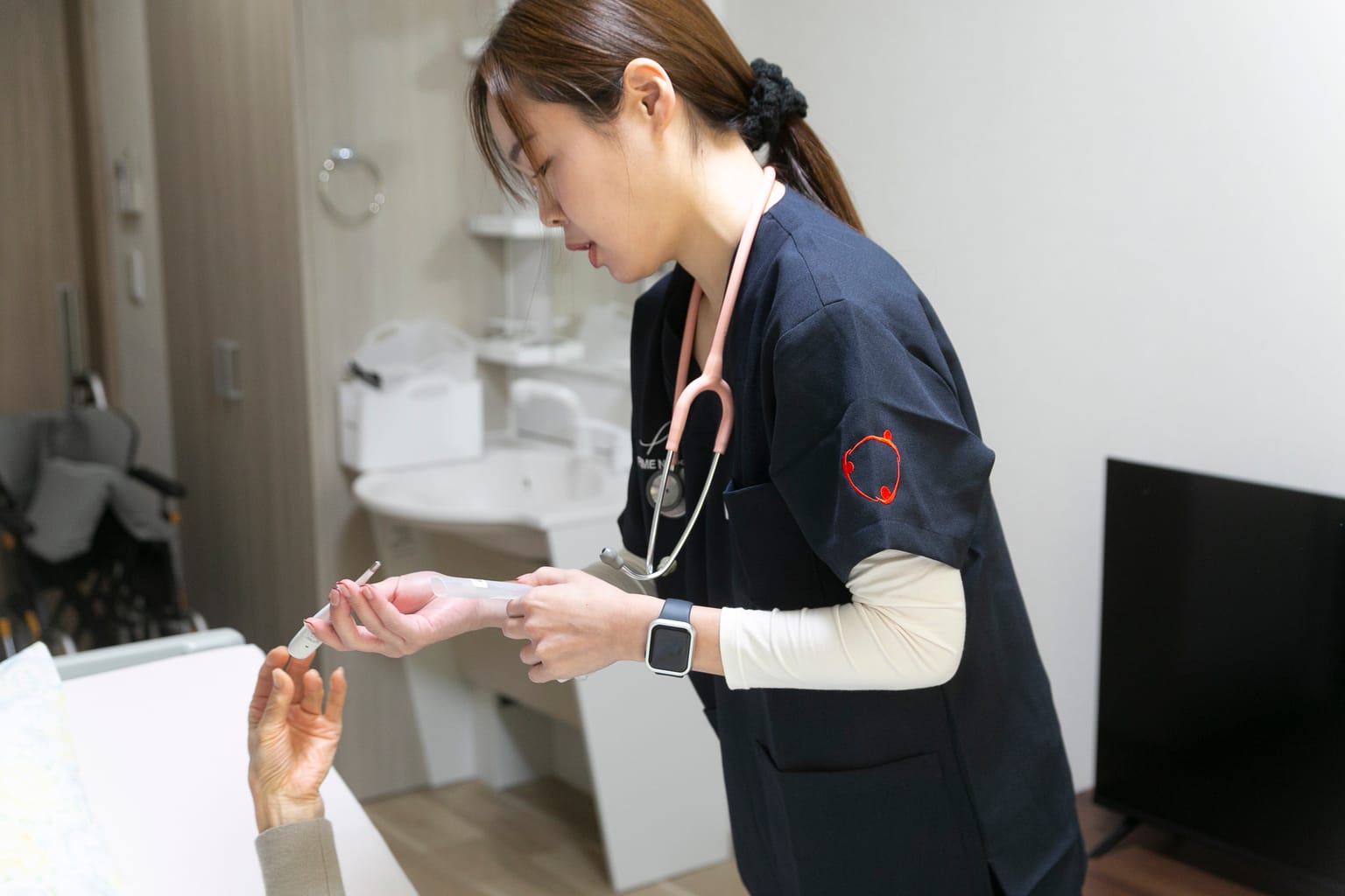 ベッドの横で利用者に手を差し出して服薬の様子を確かめる訪問看護師(関連会社3SMILEの訪問看護の撮影より)