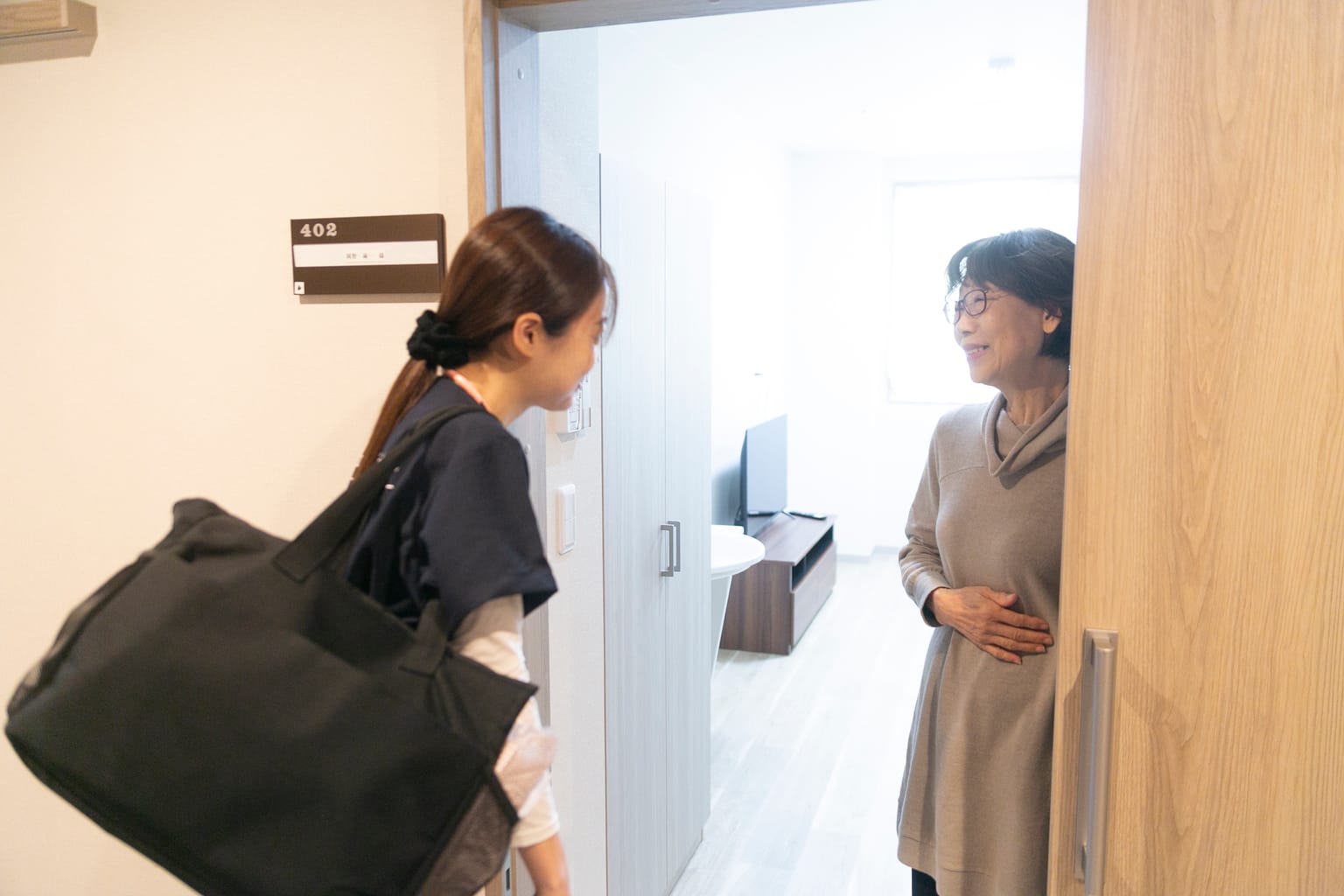 利用者の部屋の入口で、訪問看護師があいさつをしている(関連会社3SMILEの訪問看護の撮影より)