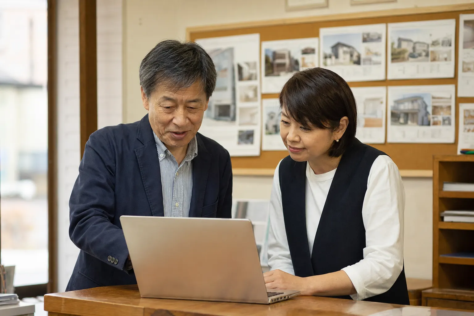 小さな不動産会社で、社長と事務員がノートパソコンを一緒に見ている（AIで生成したイメージ）