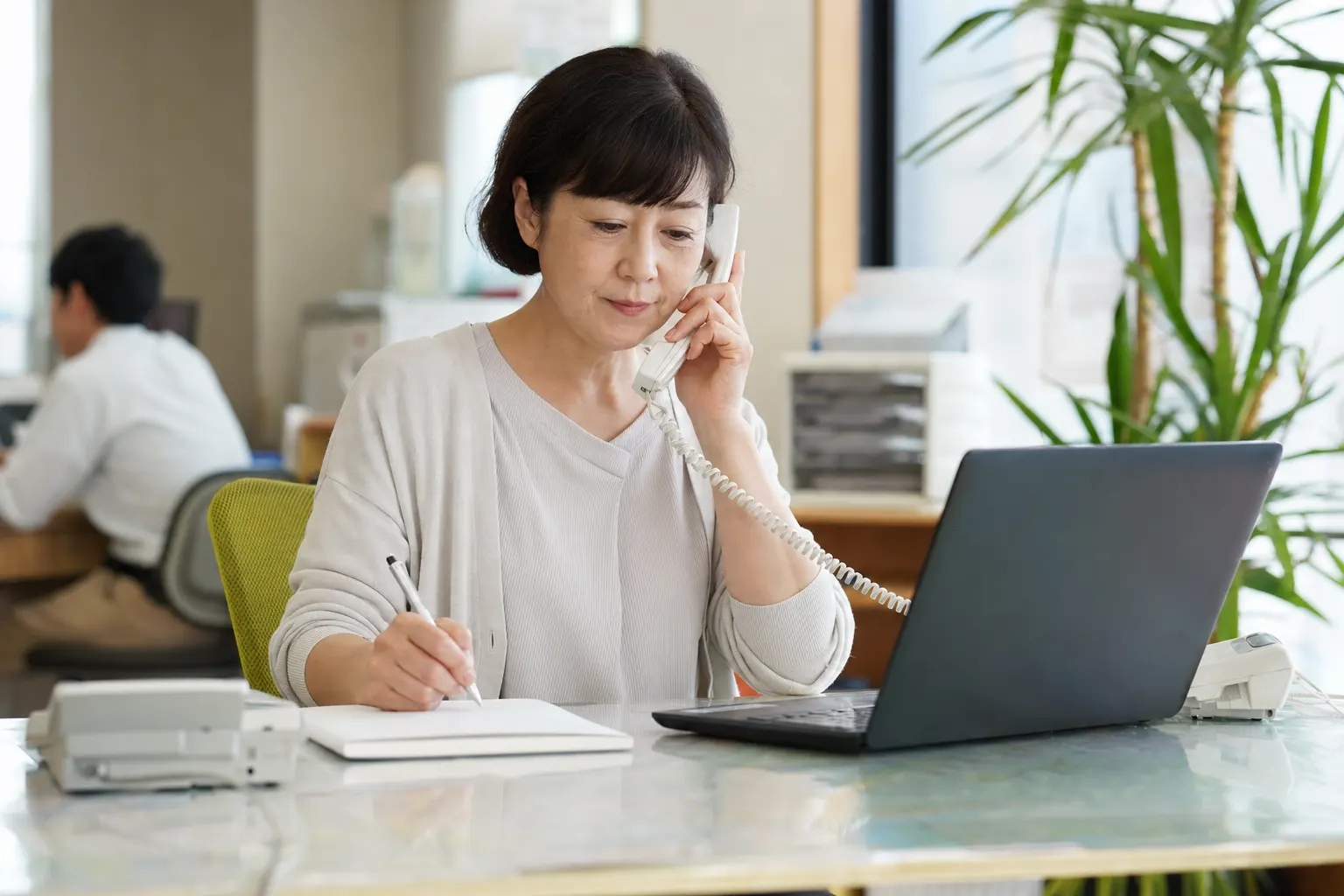 事務員が電話をしながらノートにメモを取っている（AIで生成したイメージ）