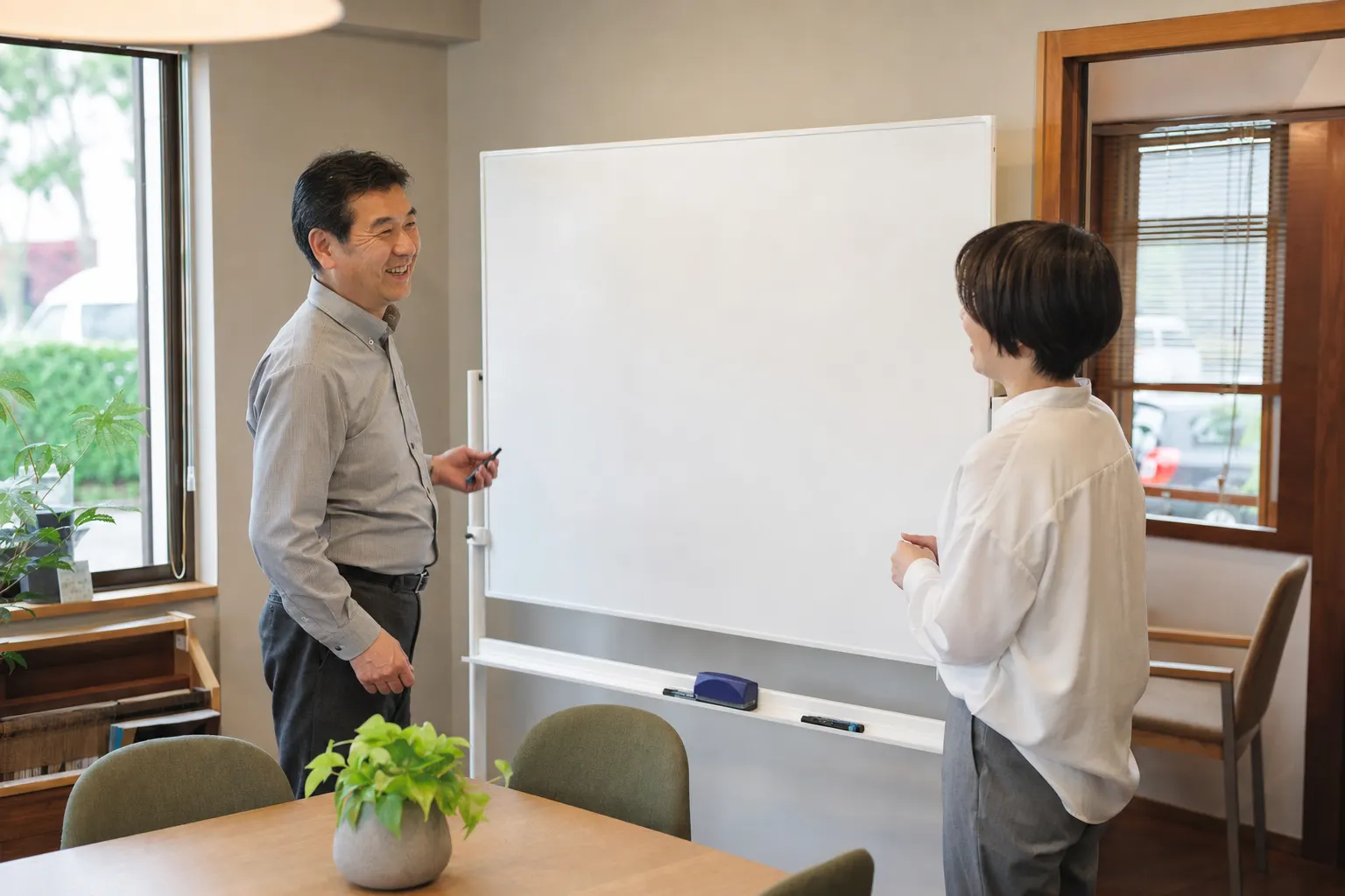小さな不動産会社で職員2人がホワイトボードの前で話している(AIで生成したイメージ)